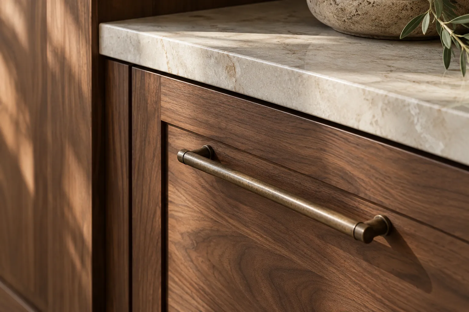 Close view of walnut drawer fronts, a brass handle and pale stone counter edge